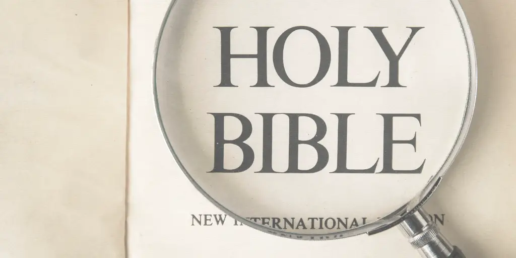 A magnifying glass highlights the words "Holy Bible" on an New International Version of the Bible.