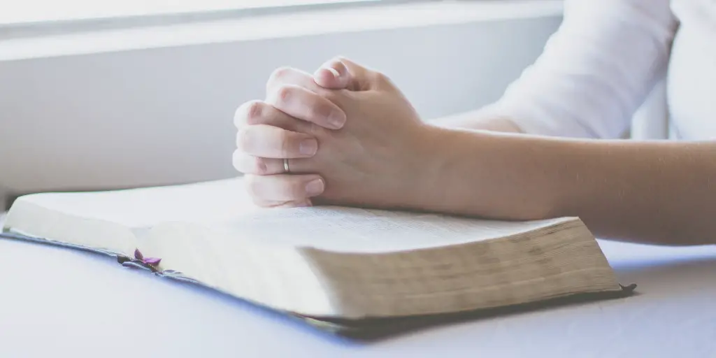 A woman prays with her hands together on top of an open bible.