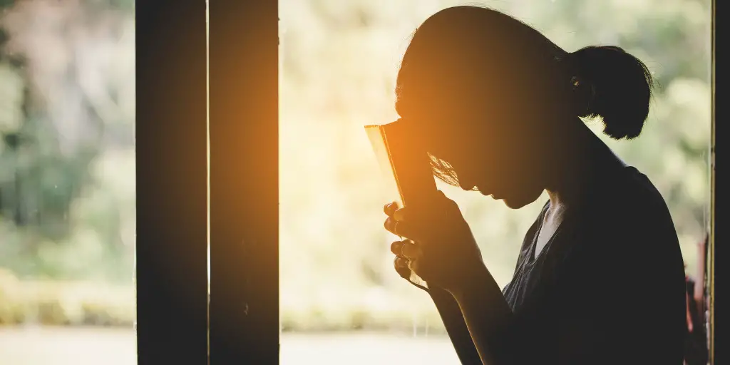 A woman holds her bible to her forehead while in prayer.