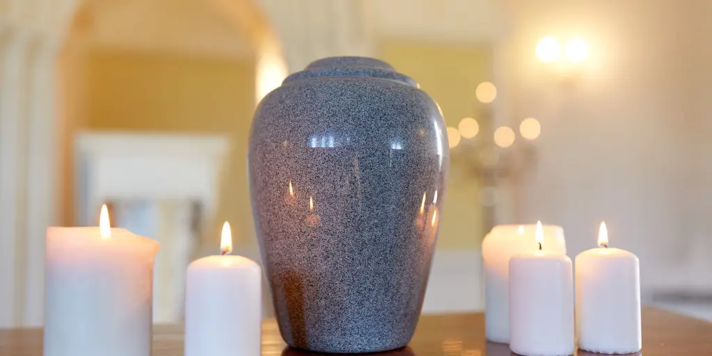 A cremation urn sits on a table amongst lit candles.