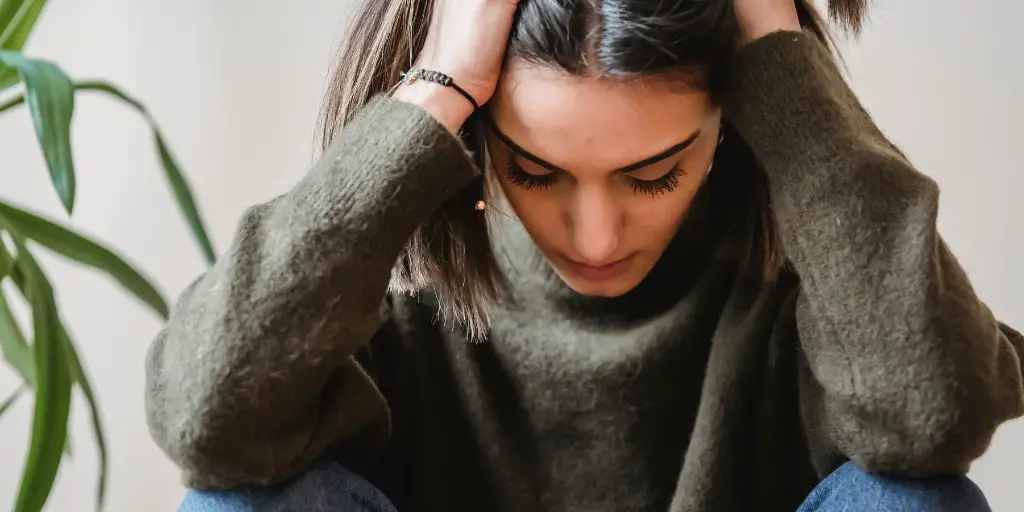 A stressed woman sits with her hands on her head.