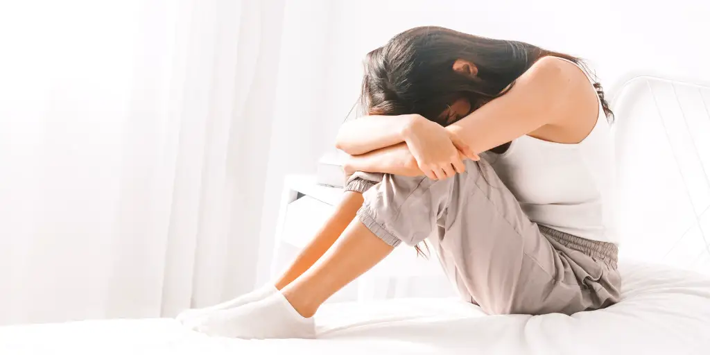 A stressed woman sits while she leans her head on her arms.