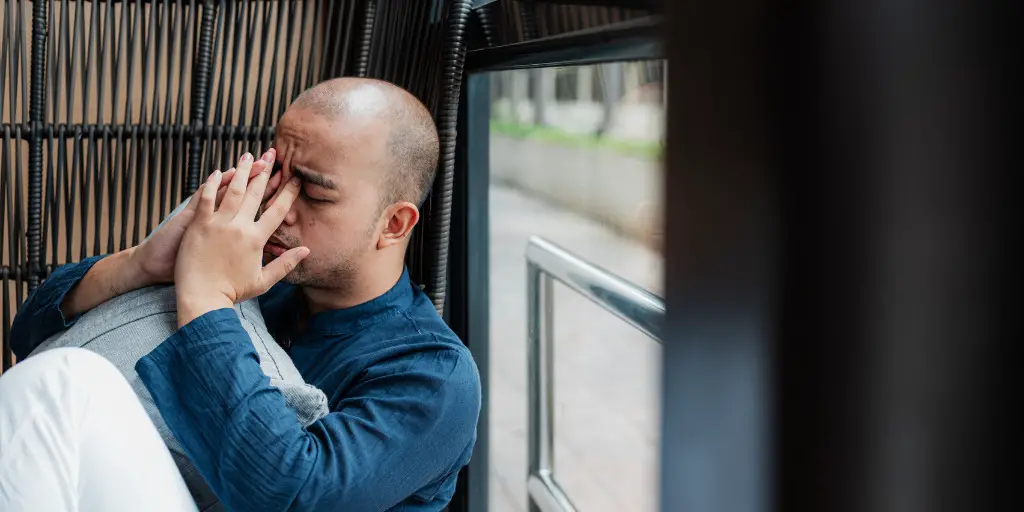 A stressed man leans against a window with his hands up to his face.
