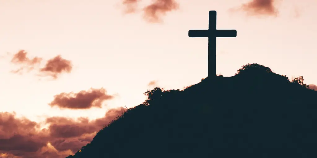 The silhouette of a cross atop a mountain.