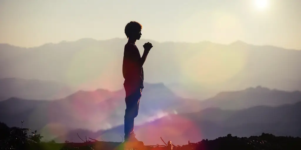 A man standing with his hands clasped appears to be praying.