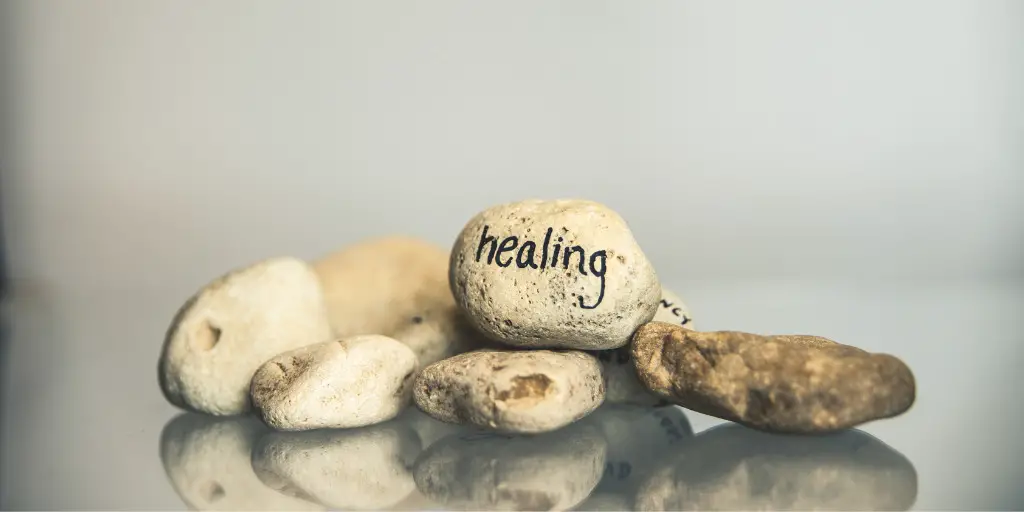 A pile of rocks lay on a table. The top rock has writing on it that reads "healing."