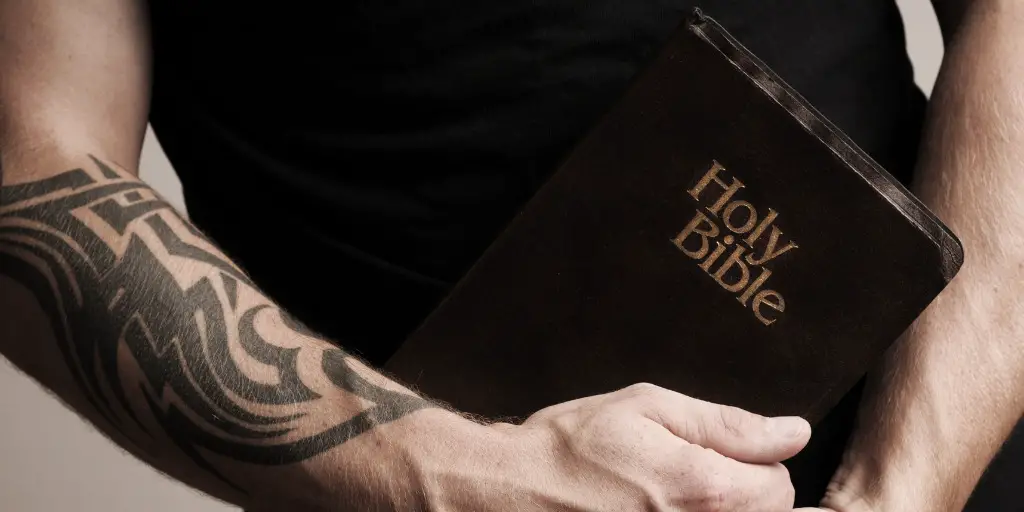 A man with a tattooed arm holds a closed bible.